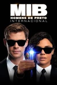 Dois agentes de óculos escuros e ternos pretos,um homem e uma mulher,em fundo escuro. Ele segura um aparelho brilhante com um pequeno alienígena.