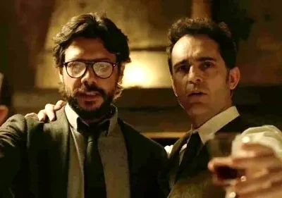 Dois homens de terno brindam com copos em ambiente escuro. Um de óculos tem expressão confiante, o outro, séria e atenta.