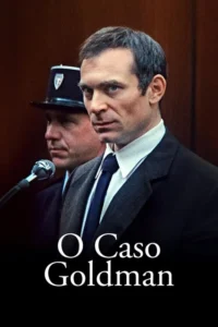 Homem de terno escuro olha intensamente. Um guarda e microfone atrás,sugerindo um ambiente de tribunal sombrio e tenso.
