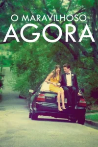 Casal em trajes de gala,ela de vestido amarelo,ele de smoking,sentados no porta-malas de um carro em rua arborizada. Clima jovem e romântico.