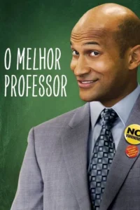 O Melhor Professor 3 Homem careca de pele escura, terno cinza, sorrindo maliciosamente. Ele tem botões divertidos na lapela contra um quadro-negro verde.