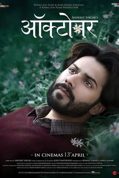 Um jovem barbudo, deitado em grama verde com pequenas flores brancas, olhando para cima com expressão pensativa e serena.