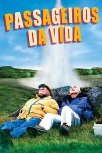 Dois idosos sentados na grama, olhando para um gêiser em erupção em um campo verde. Céu azul e paisagem natural.