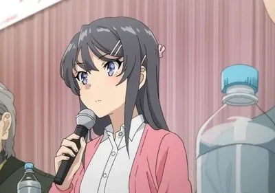 Mulher anime de cabelo escuro, camisa branca e casaco rosa, segura microfone com expressão séria. Outras pessoas e garrafas de água.