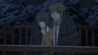 Um casal de anime em casacos grossos está em uma varanda nevada à noite. O garoto olha para frente, a garota para baixo, com árvores escuras ao fundo.