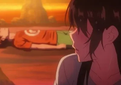 Mulher suada e em prantos olha para homem caído no chão, sob um pôr do sol laranja e vermelho intenso.