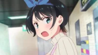 Anime girl com cabelo curto preto, laço azul e olhos teal arregalados. Bochechas coradas, boca aberta em surpresa, em um corredor claro.