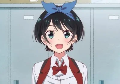 Jovem anime de cabelo curto e laço azul, sorrindo abertamente, com bochechas rosadas. Veste camisa branca. Fundo de armários escolares.