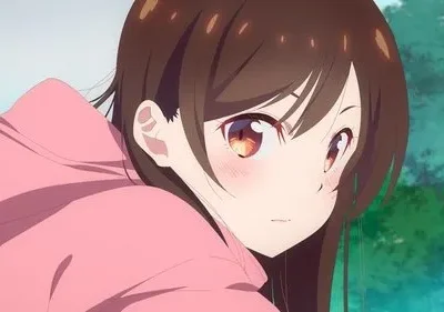 Jovem anime de cabelo castanho e moletom rosa, com bochechas coradas, olhando para o lado. Fundo suave com vegetação.