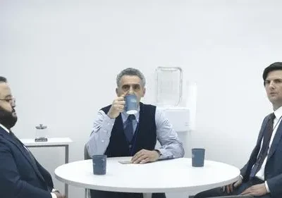 Três executivos em ternos escuros numa sala branca minimalista. Um bebe, outro observa, e o terceiro encara. Ambiente tenso.