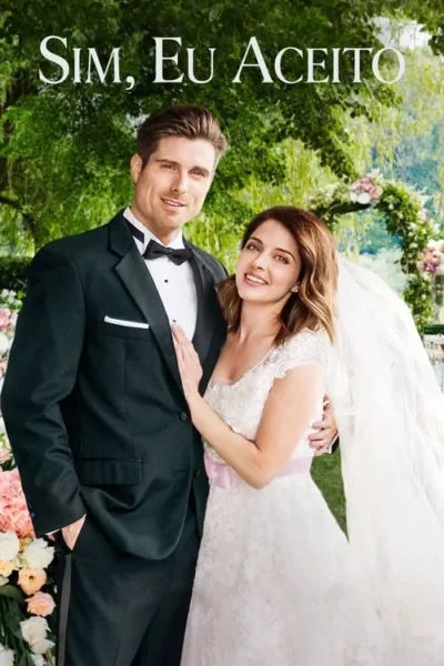 Casal sorridente em roupas de casamento, ele de terno, ela de vestido branco com véu. Abraçados num jardim florido com arco. Clima romântico.