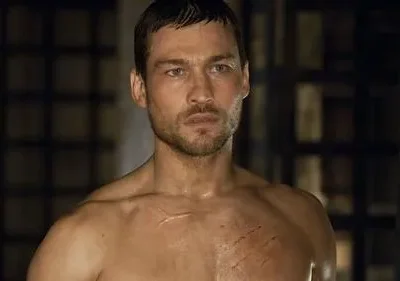 Homem musculoso, sem camisa, com olhar sério e cicatrizes no peito. Fundo escuro com grades. Clima de luta e resiliência.