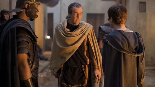 Spartacus – T01E11:Feridas Antigas 1 Três figuras em trajes antigos. Um soldado romano e um homem de toga conversam com uma pessoa de costas numa rua escura.