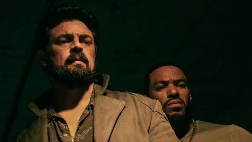 The Boys – T01E04:A Fêmea da Espécie 1 Homem barbudo com casaco marrom e cicatriz no rosto,olhando sério. Outro homem espreita por trás na penumbra verde.