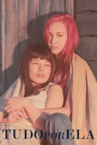 Duas mulheres abraçadas:uma com cabelo rosa e olhar direto,outra sorrindo com franja. Fundo de madeira e luz quente.