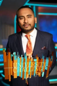 Pôster: Homem barbudo de terno escuro e gravata laranja em estúdio de TV futurista azul e vermelho. Blocos gráficos vibrantes em primeiro plano.