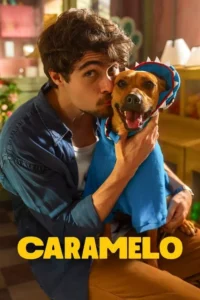 Um homem beija afetuosamente um cão marrom alegre,que veste um moletom azul de tubarão. Cena quente e feliz em ambiente interno.