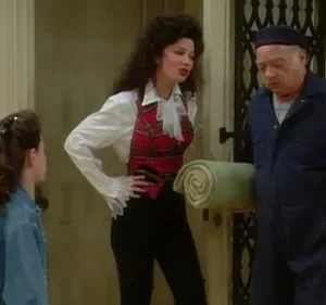 Três pessoas em um hall. Mulher com colete xadrez e menina observam homem de macacão azul com cobertor e caixa de ferramentas.