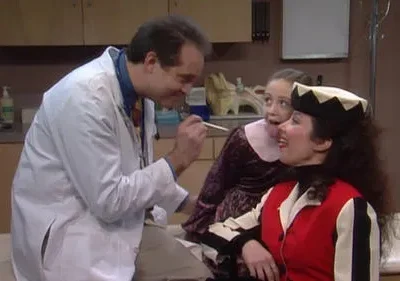 Médico sorridente, mulher em fantasia colorida e menina travessa que mostra a língua, num consultório. Clima divertido e humorístico.