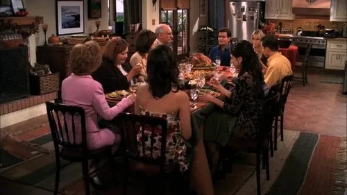 Dois Homens e Meio – T01E10:Feliz Ação de Graças 1 Pessoas reunidas em um jantar festivo,com mesa farta e peru. Cenário de lar aconchegante com cozinha e lareira visíveis.