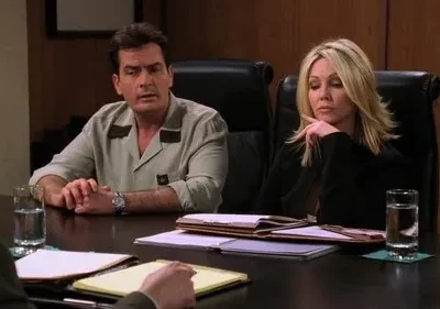 Homem e mulher em reunião séria. Ele fala, ela está pensativa na mesa de conferência com documentos e copos d'água.