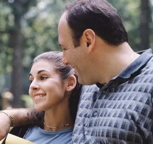 Um homem sorrindo com o braço em volta de uma jovem sorridente. Cenário de parque verde ao fundo. Uma cena feliz e afetuosa.