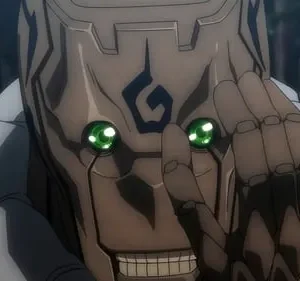 Rosto marrom, tipo madeira/máscara, com olhos verdes brilhantes e sorriso sinistro. Mão articulada escura perto do rosto. Floresta desfocada.