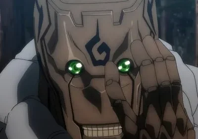 Rosto marrom, tipo madeira/máscara, com olhos verdes brilhantes e sorriso sinistro. Mão articulada escura perto do rosto. Floresta desfocada.