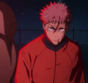 Jovem de cabelo rosa espetado, rosto ferido e expressão séria, sob forte luz vermelha. Fundo noturno escuro com grades.