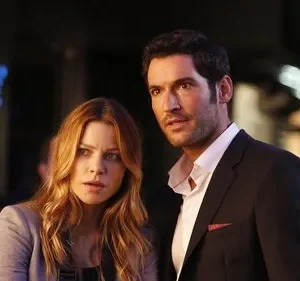 Um homem de terno e uma mulher com expressões tensas/surpresas, em uma cena noturna urbana com luzes desfocadas ao fundo.