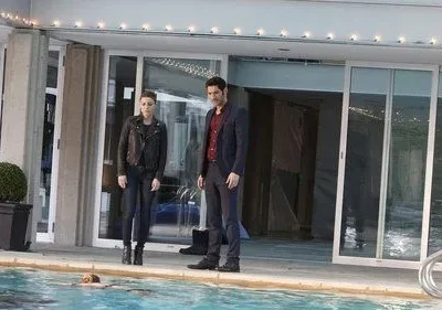 Homem de terno e mulher de jaqueta preta observam uma pessoa flutuando na piscina de uma casa moderna. Clima tenso.