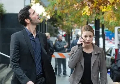 Homem de terno olhando para cima, mulher ao telefone com expressão séria em rua movimentada. Clima urbano e tenso.