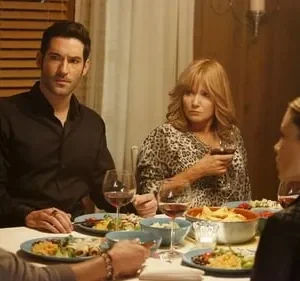 Quatro pessoas jantam. Homem de preto olha intenso; mulher de estampa de leopardo observa preocupada, com taça de vinho.