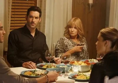 Quatro pessoas jantam. Homem de preto olha intenso; mulher de estampa de leopardo observa preocupada, com taça de vinho.