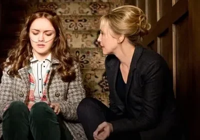 Uma jovem com cânula nasal e uma mulher adulta estão sentadas em uma escada. A adulta a observa. Clima sério e preocupante.