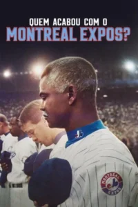 Homem negro de cabelo grisalho em uniforme de beisebol listrado com gola azul olha para baixo em campo noturno iluminado. Clima sério.