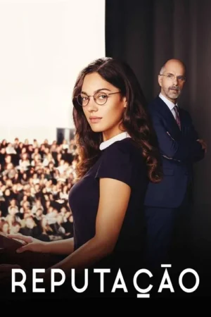 Mulher de óculos, cabelos escuros, olhando séria. Homem em terno, braços cruzados, ao lado. Plateia borrada ao fundo. Ambiente formal.