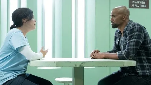Mulher gesticula para homem em mesa de sala institucional verde. Ele ouve pensativo. Clima de conversa séria ou interrogatório.