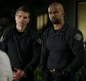 Três policiais (dois homens, uma mulher) em uniformes táticos pretos encaram uma pessoa de costas. Clima sério à noite.