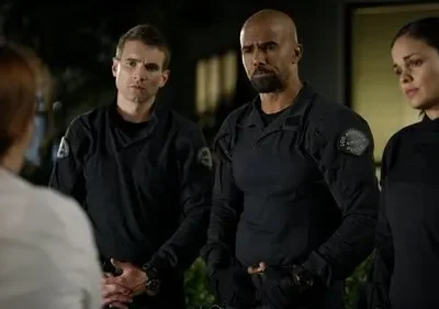 Três policiais (dois homens, uma mulher) em uniformes táticos pretos encaram uma pessoa de costas. Clima sério à noite.