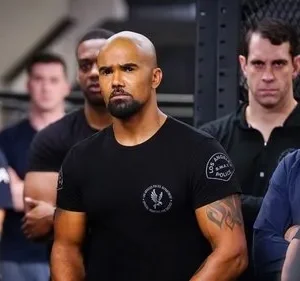 Homem negro musculoso de camiseta preta SWAT em destaque, entre outros homens sérios em ambiente interno. Clima profissional e tenso.