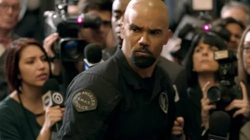 S.W.A.T.:Força de Intervenção – T01E19:Fonte 1 Um policial SWAT careca e barbudo,com expressão séria,em meio a uma multidão de jornalistas com câmeras e microfones.