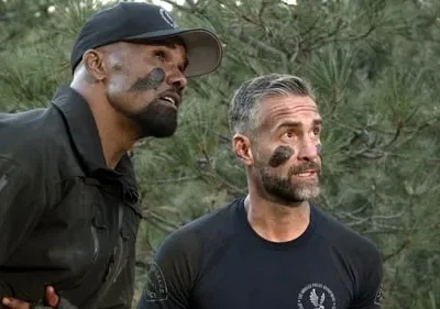 Dois homens vigilantes com pintura de camuflagem olham para cima em uma floresta. Um de boné e uniforme tático, o outro de camiseta.