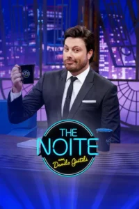 Homem de terno e barba, com olhar maroto, segura caneca preta. Cenário de cidade noturna em tons azuis. Clima de talk show.