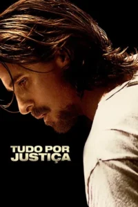 Um homem barbudo de cabelo comprido olha para baixo com expressão séria. A iluminação dramática destaca seu perfil contra o fundo escuro.