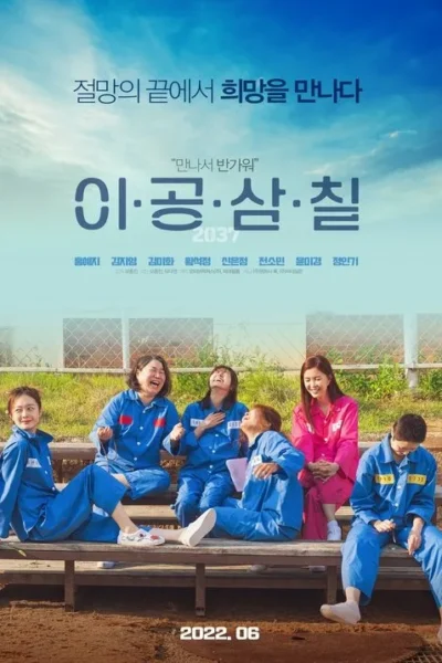 Seis mulheres, cinco de uniforme azul e uma de rosa, riem juntas num pátio cercado sob céu azul, transmitindo camaradagem e esperança.