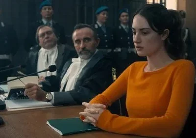 Mulher séria de suéter laranja sentada em tribunal. Juízes e policiais ao fundo. Clima de drama legal e tensão.