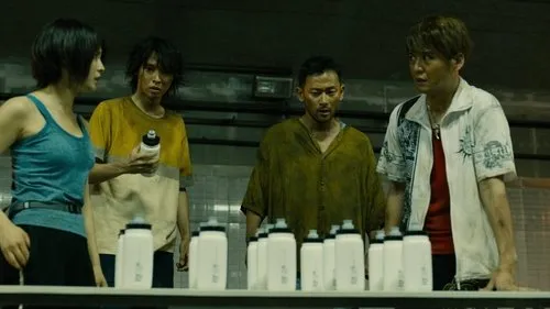Alice in Borderland – T01E04:Episódio 4 1 Quatro personagens (3 homens,1 mulher) com expressões tensas olham garrafas em sala industrial escura. Clima de desafio.