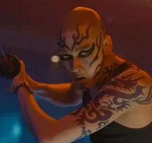 Pessoa careca com pintura facial e tatuagens, empunhando uma katana em pose de combate, sob luzes neon dramáticas.