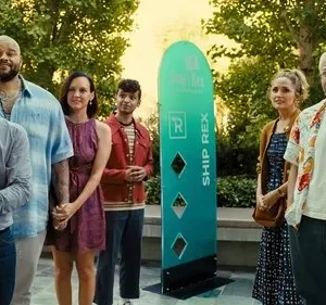 Seis pessoas sorridentes, de diversas etnias, posam em um ambiente externo ensolarado com banners coloridos. Clima alegre e casual.